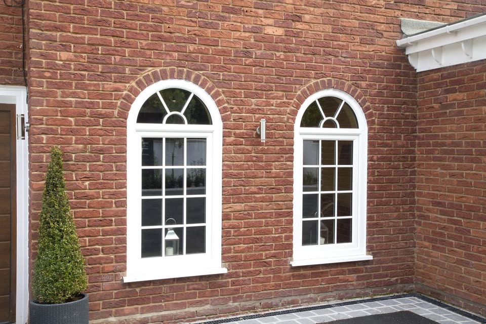 Two arched white uPVC windows with Georgian bars in a brick wall