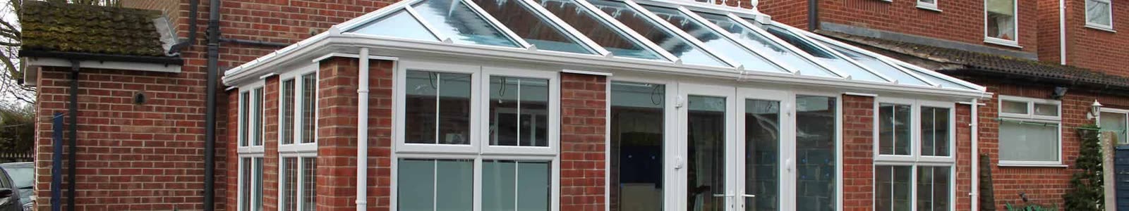 Long white uPVC conservatory with a glazed roof on a brick house