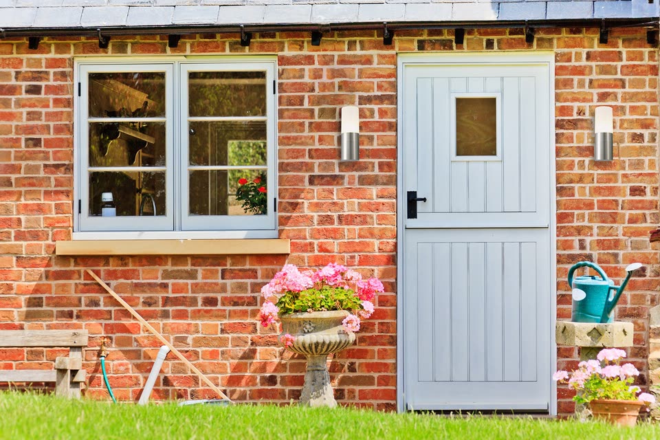 Grey stable door and matching window on a brick cottage