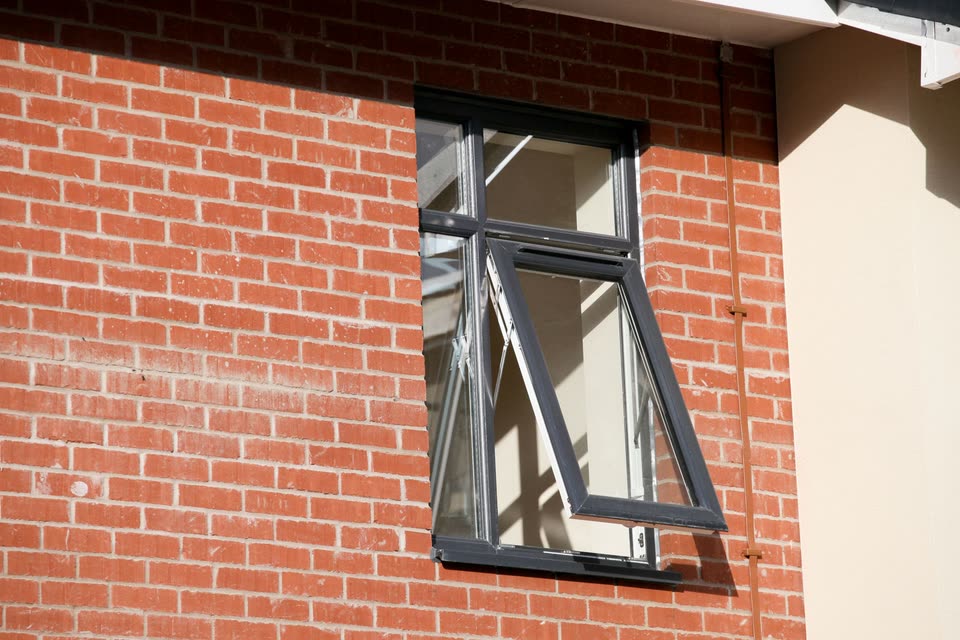 Grey tilt and turn window tilted open in a brick wall
